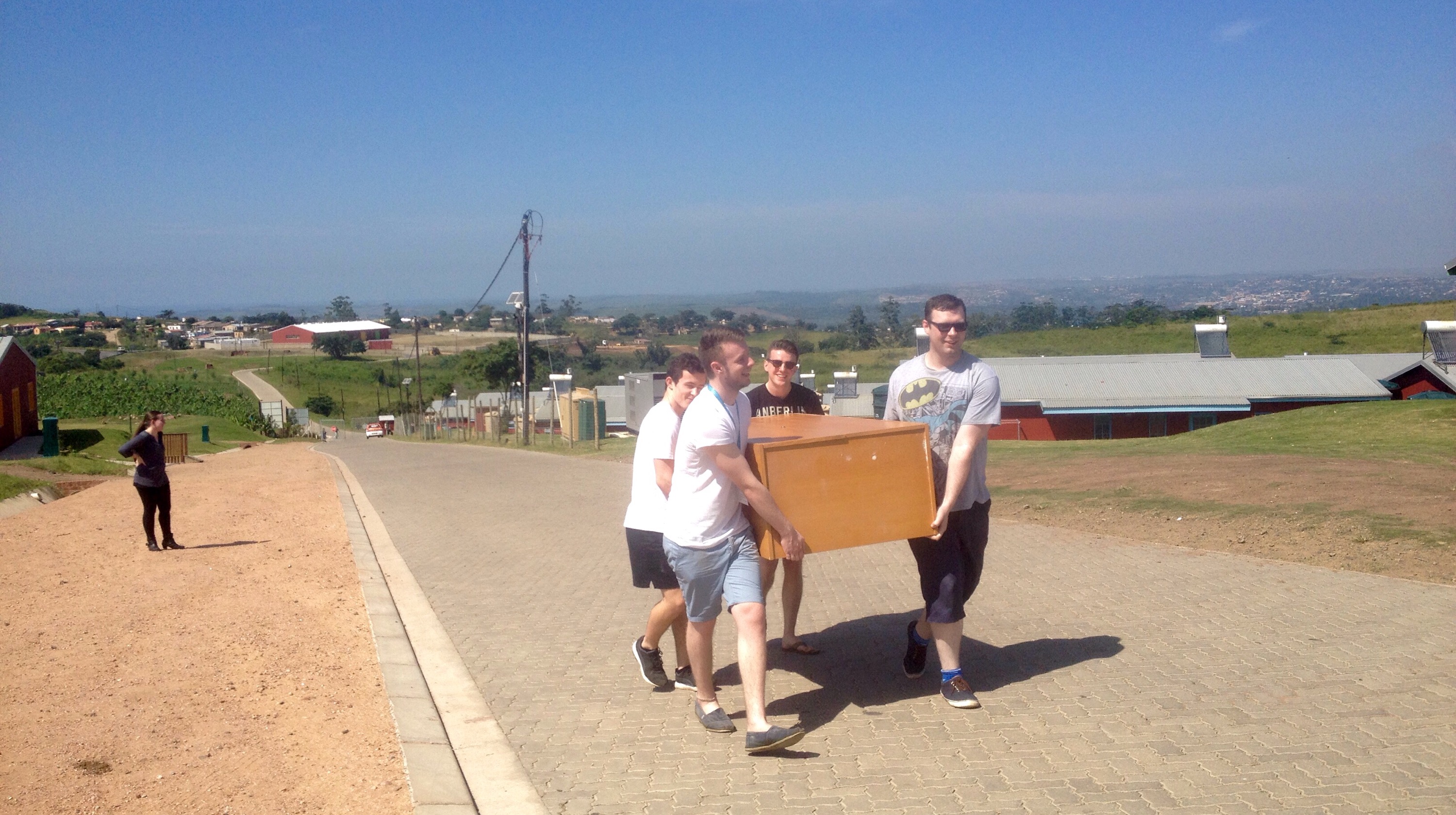 Four people carrying a wardrobe up a hill